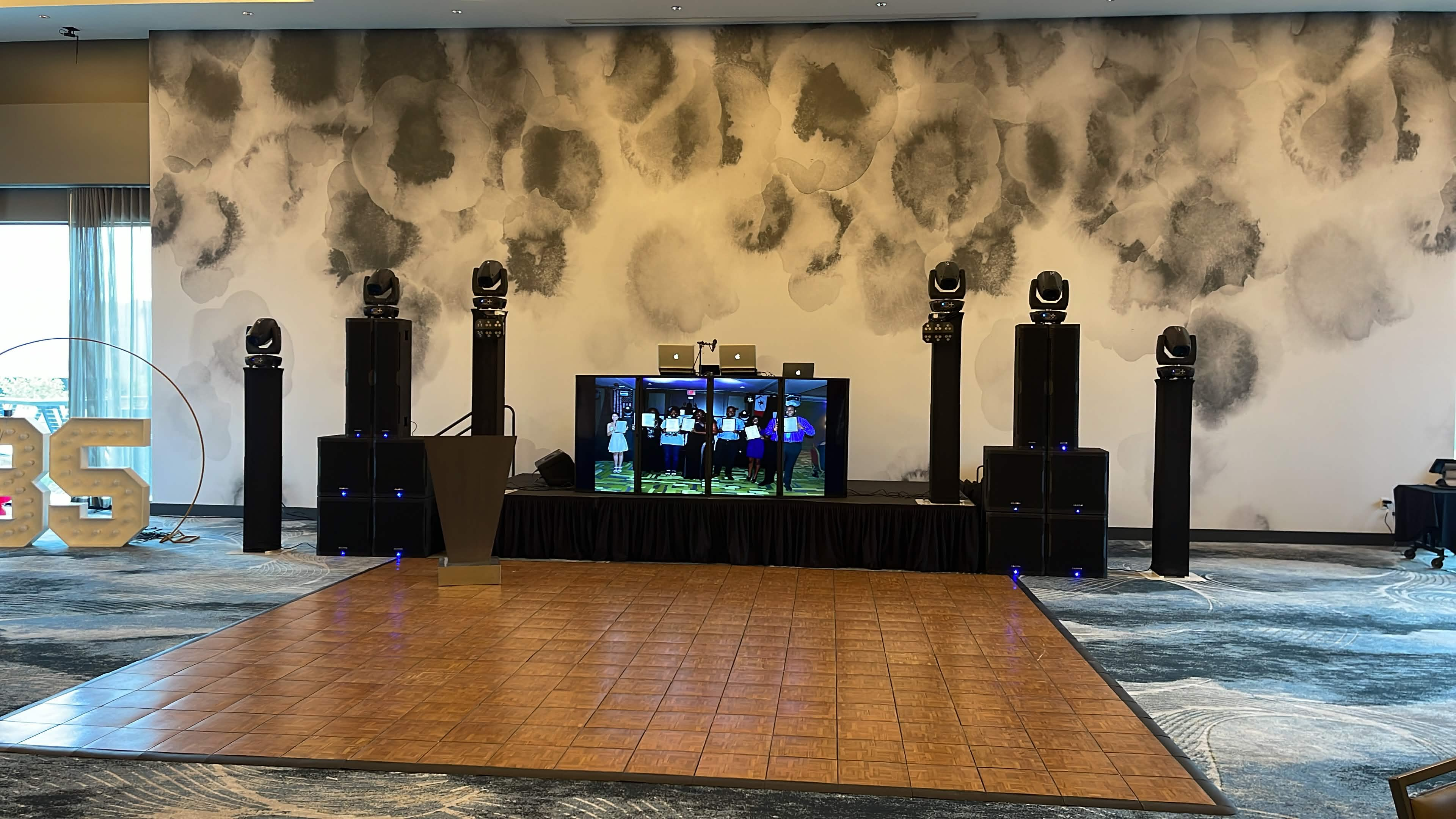 Large ballroom DJ stage with multiple speaker stacks, moving lights, and dance floor