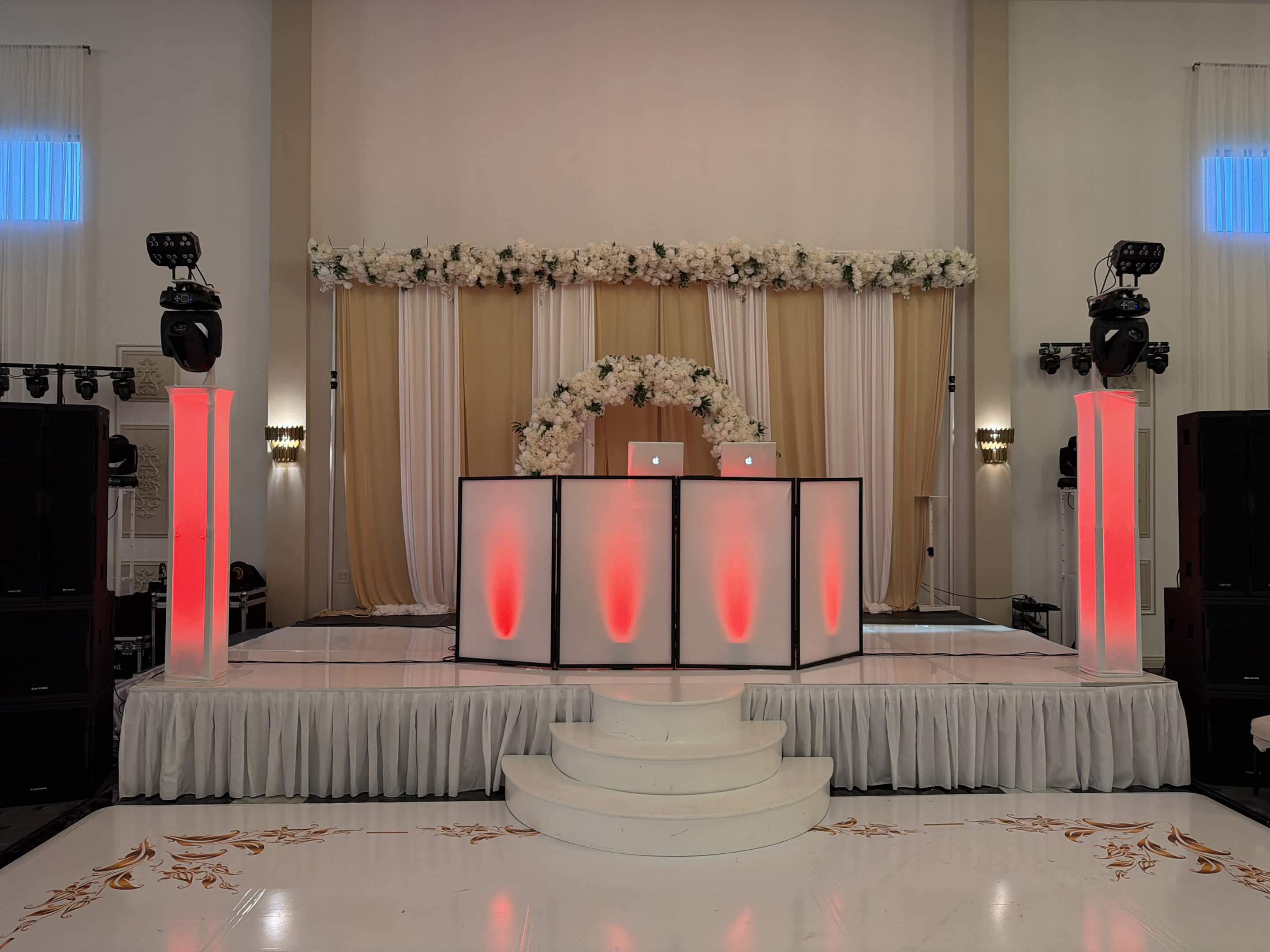 Elegant wedding DJ booth with coral-lit columns and floral backdrop
